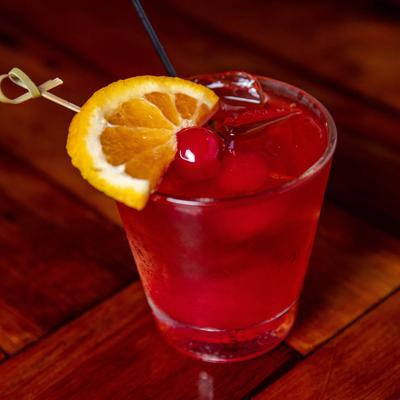 Red drink sits on a wooden suraface, garnished with cherries and a lemon slice.
