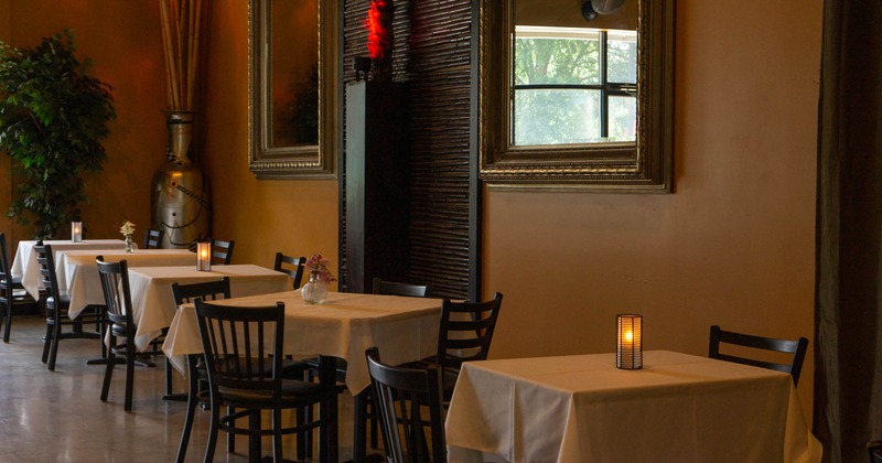 Interior, dining area, white cloth tables for four, flower vases and candles as a centerpieces