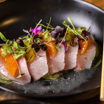 Hamachi carpaccio with citrus slices and microgreens.