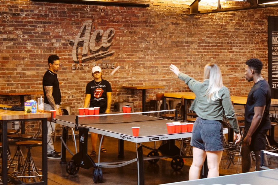 Interior, a group of guests playing table tennis with cups on the table.