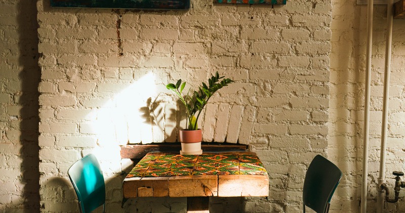 A small wooden table with a mosaic top and teal chairs in a room with white brick walls