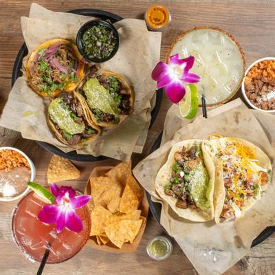 Plates of tacos on corn and flour tortilla, beans and rice, pink drink and yellow drinkall viewed from above.