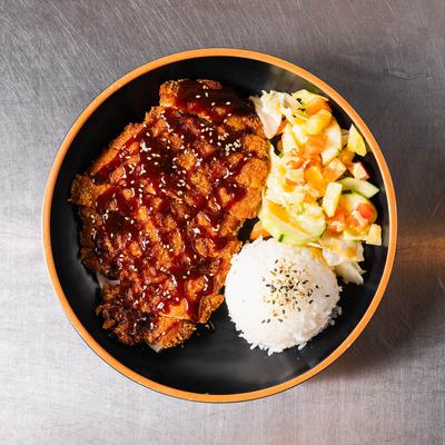 Breaded and fried chicken served with rice, vegetables, and tonkatsu sauce.