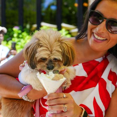 A customer smiles while holding a small fluffy dog, the dog is enjoying a treat.