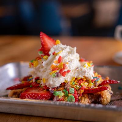 Waffle topped with whipped cream, strawberries and fruit pebbles.