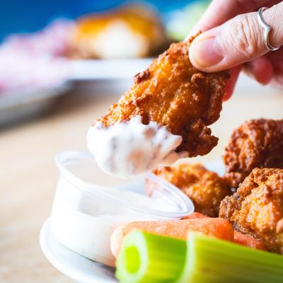 A hand dipping a wing ding into ranch sauce.