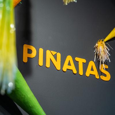 Pinatas sign with yellow lettering on a dark wall with party decorations.