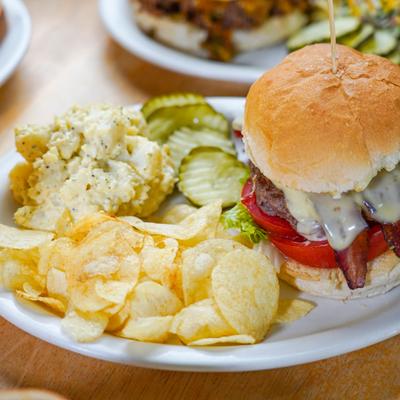 Bacon cheeseburger served with chips, potato salad and pickles.