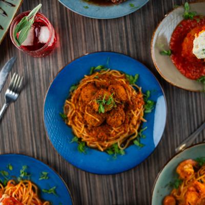 Meatball spaghetti surrounded by other Italian dishes and a cocktail.