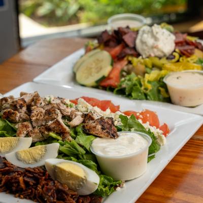 Two large plates of loaded chicken salads with creamy dressing on top.