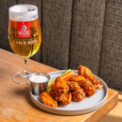 Plate of wings with vegetable sticks and a dip, served with a glass of beer.