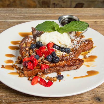 French toast with whipped cream, berries, granola and caramel drizzle on white plate