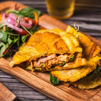 Crispy green plantain sandwich with grilled chicken, served with lettuce, tomato, and red onions.