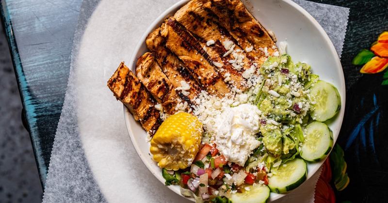 Rice bowl with grilled chicken, rice, beans, salsa, sour cream, and corn