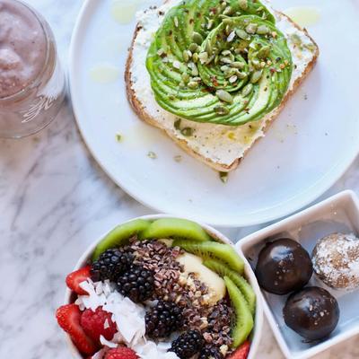 A healthy breakfast spread featuring avocado toast, a fruit bowl, and energy balls.