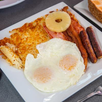 Breakfast plate featuring fried eggs, sausages, bacon, hash browns and pineapple.