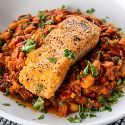 Salmon served over a stew of white beans and tomatoes, garnished with herbs.