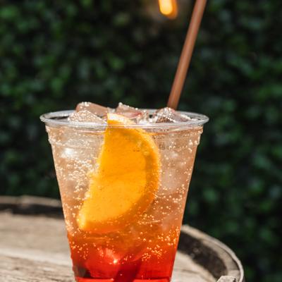 Aperol Spritz served in a plastic cup with orange slice garnish.