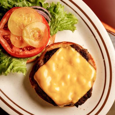 An open-faced cheeseburger with pickle slices, tomato, and lettuce, served on a plate.