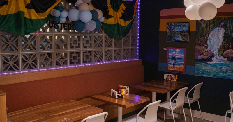 Interior of a café with wooden tables, white chairs, colorful wall art, and festive balloons