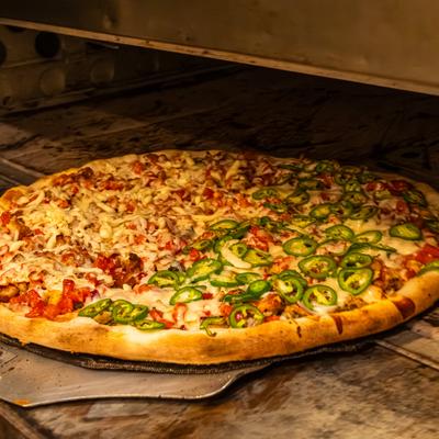 Large half-and-half pizza baking in an oven with cheese, tomatoes, and jalapenos.