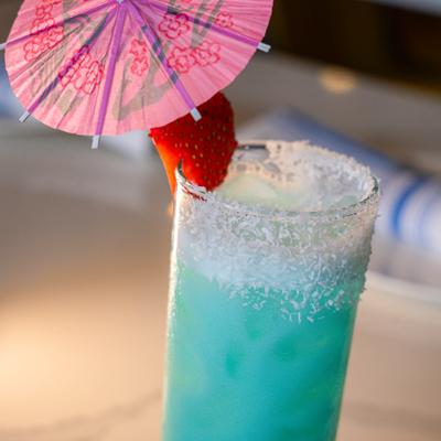 Blue cocktail with a coconut rim garnished with a strawberry and a paper umbrella.