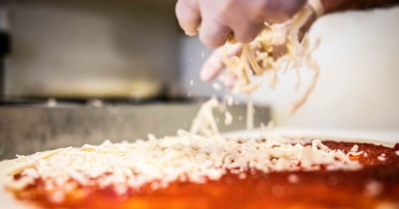 Hands putting cheese on pizza dough with sauce spread on it