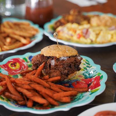 A plated fried chicken sandwich on a cornbread bun, served with sweet potato fries.