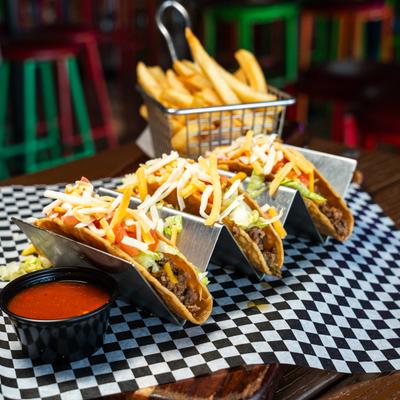 Tacos served with red salsa, accompanied with fries in the background.