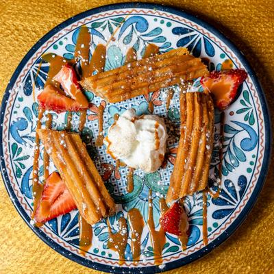 Churros served with vanilla ice cream, sliced strawberries, and a caramel drizzle.