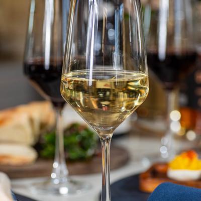 A glass of white wine surrounded by food plates and wine, close up.