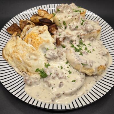 A plate of biscuits topped with creamy sausage gravy, home fries, and fried eggs.