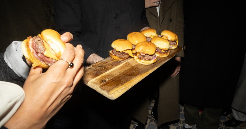 A hand holding a slider beside a server offering more on a wooden board