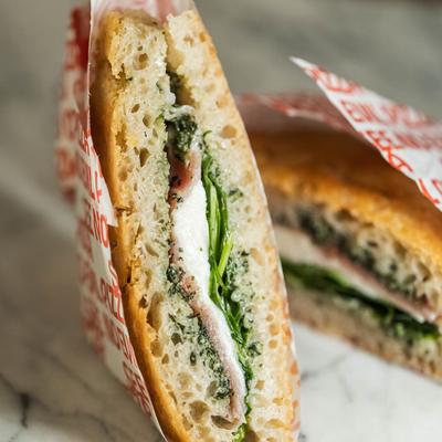Sandwich with prosciutto, mozzarella, pesto, and arugula.
