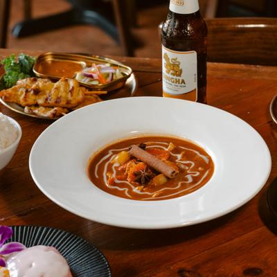 Massaman curry bowl sits on a restaurant table with beer and other dishes.