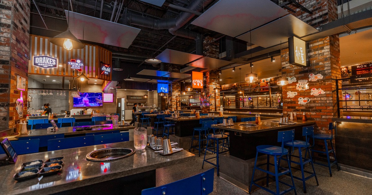 Interior of a modern restaurant with built-in grill tables, blue stools, brick walls