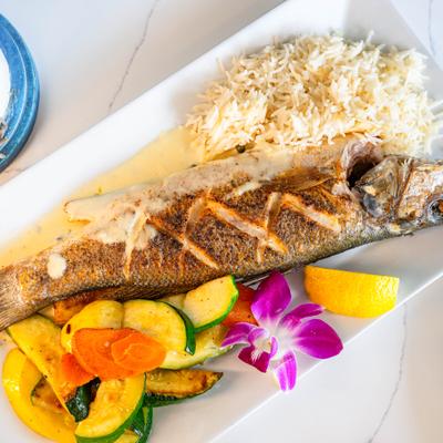 Grilled branzino with rice, sauteed vegetables, and orchid garnish.