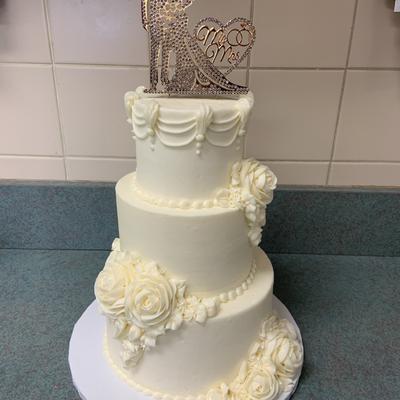 A three tiered white cake with white floral decorations wedding cakes