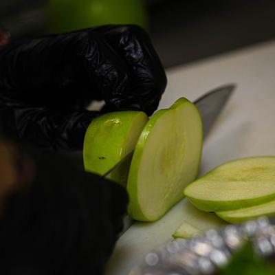 Hands in black gloves slicing an apple.