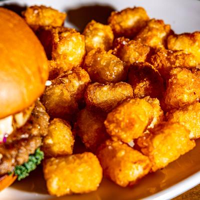 Burger served with tater tots, close-up.