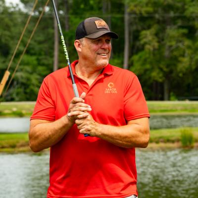 Person holding a fishing rod with lake in the background.