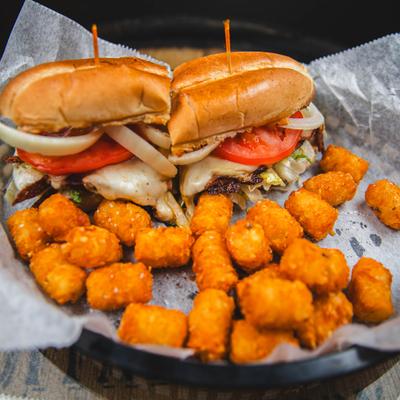 Chicken sandwich with cheese, lettuce, tomato, onion and a side of tater tots.