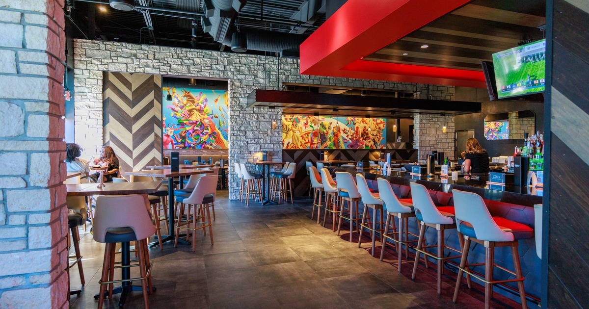 Modern restaurant interior with a bar, stools, tables, colorful murals