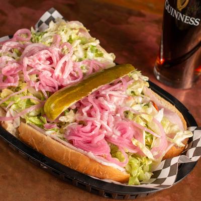 Deli Sub sandwich topped with lettuce, pink onions, and a pickle.