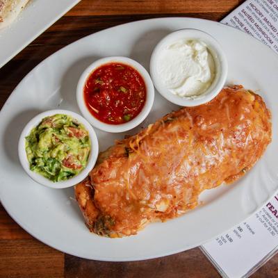 Breakfast burrito with guacamole, red salsa, and sour cream, top view.