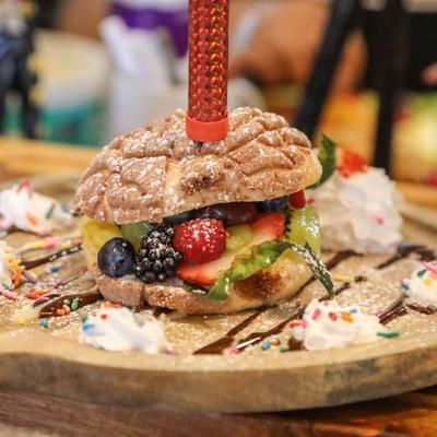 Dessert sandwich filled with fresh fruit, garnished with whipped cream and sprinkles.