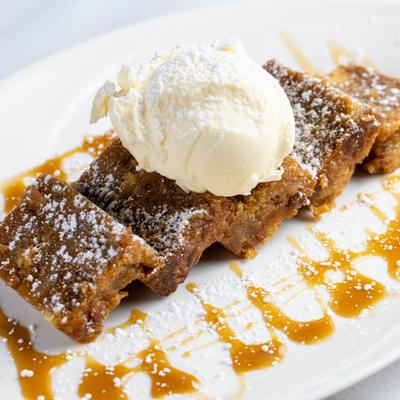 Bread pudding topped with ice cream, powdered sugar, and caramel drizzle.