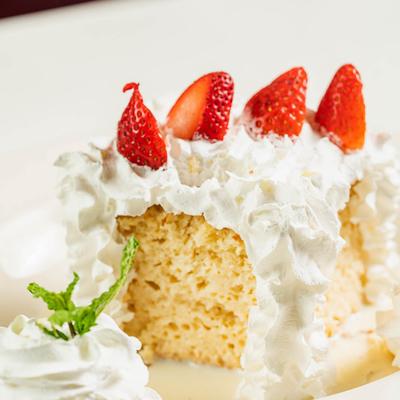 Tres Leches cake covered with whipped cream, topped with sliced strawberry