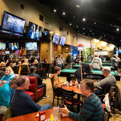 Interior with multiple pool tables, large television screens and people seated.