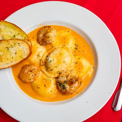 Lobster shrimp ravioli in creamy orange sauce served with garlic bread slices.